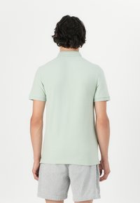 Light green short-sleeve polo shirt made of soft fabric, featuring a ribbed collar and cuffs, paired with striped shorts. Plain back view.