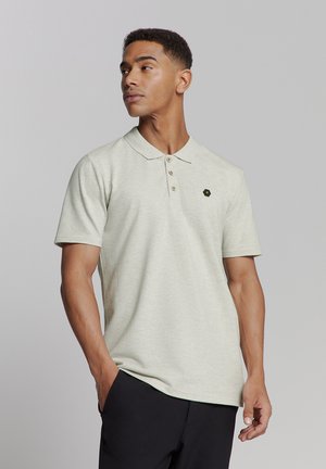 Lichtgrijze polo met een zachte textuur, drie knopen en een klein donker embleem op de linkerkant van de borst. Korte mouwen en een klassieke kraag.