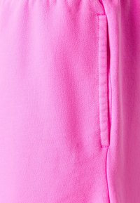 Tissu en polaire rose clair avec une texture lisse, ceinture élastique et une poche latérale. Le design est décontracté et simple.