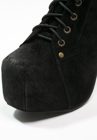 Botte plateforme en daim noir avec bout arrondi, lacets noirs, œillets métalliques et détail de rivet doré.