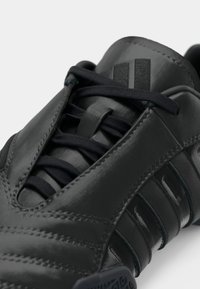 Mørkegrå treningsko med glatt skinnfinish, teksturerte detaljer, mesh-tunge og flate svarte lisser. Har logo-detaljer.