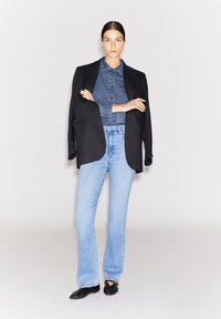 Schwarzer Blazer kombiniert mit einem Denim-Hemd, hellblauen Schlagjeans und schwarzen Ballerinas. Die Kleidung weist verschiedene Texturen und Farbkontraste auf.