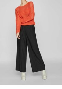 Ljust orange stickad tröja med lös passform, kombinerad med svarta vida byxor och krämfärgade plattformstövlar. Texturerad tyg och avslappnad siluett.