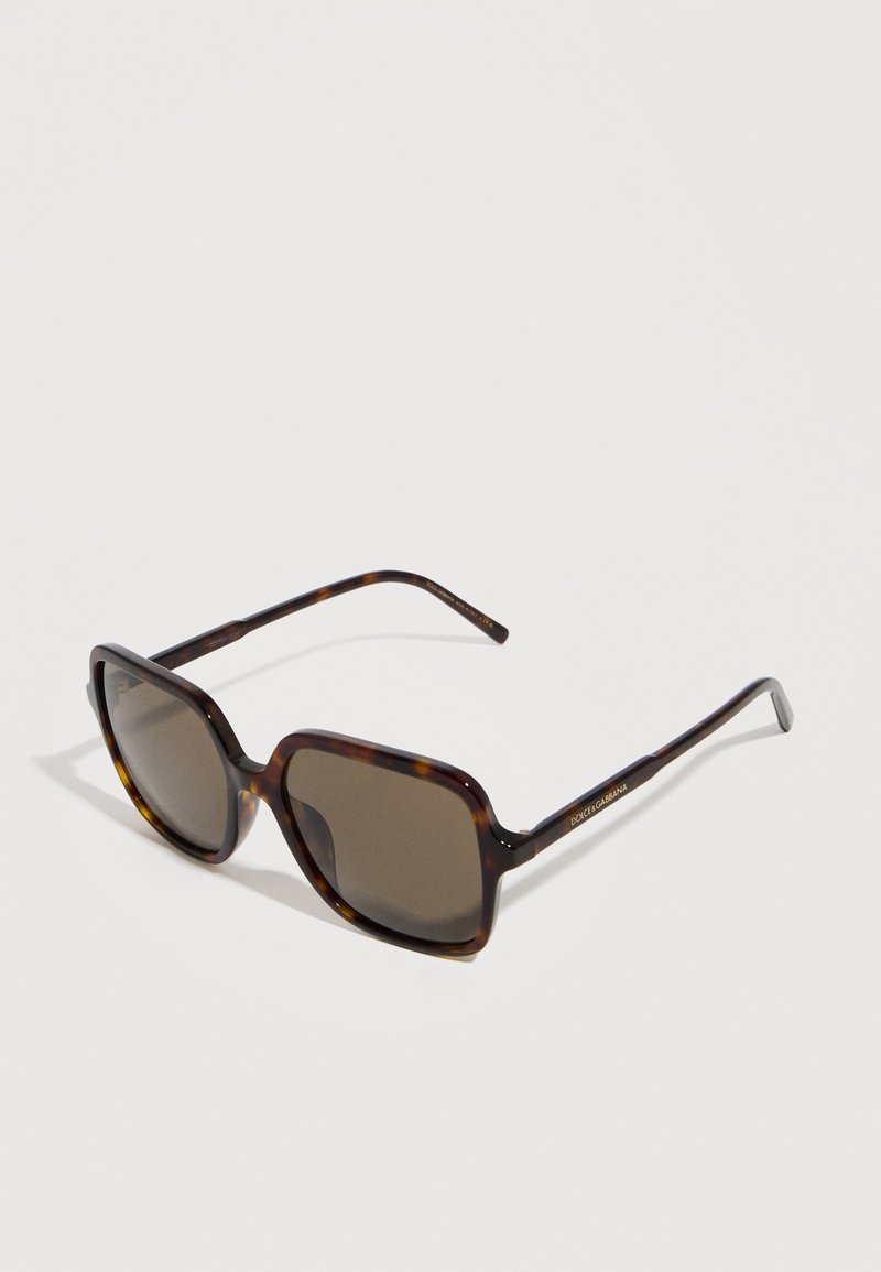 Τετράγωνα γυαλιά ηλίου με μαύρους φακούς και λεπτούς βραχίονες, με το όνομα της μάρκας ορατό στο πλάι.