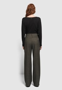 Top nero a maniche lunghe con scollatura ampia abbinato a pantaloni grigi a vita alta e gamba larga, caratterizzati da una leggera texture e tasche posteriori.