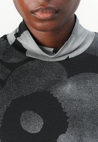 Black turtleneck sweater featuring a gray floral pattern, smooth texture, and contrasting collar detail. Close-up view of upper torso.