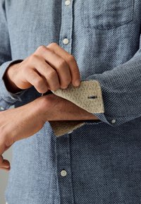 Plava košulja s uzorkom i suptilnom teksturom, s kontrastnim bež podstavom manšete ukrašenom dekorativnim uzorkom i detaljem s gumbom.