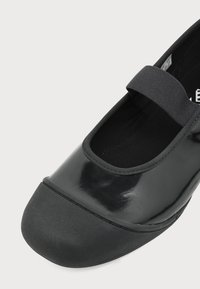 Μαύρο γυναικείο παπούτσι Mary Jane με γυαλιστερό επάνω μέρος, στρογγυλεμένη μαλακή μύτη και ελαστικό λουράκι πάνω από το πέλμα.