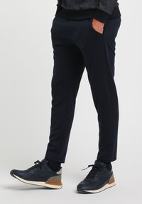 Marineblå sweats med en tapered design, der har sidelommer og en glat tekstur, sammen med marineblå og grå atletiske sko.
