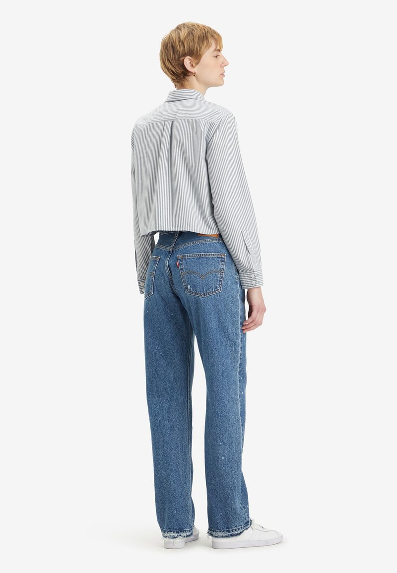 Camicia a righe, corta, con bottoni di colore blu chiaro e bianco; abbinata a jeans in denim blu a taglio largo. Sneakers bianche completano il look.