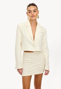 Geknipte crèmekleurige blazer met een enkele knopsluiting, notched lapels en lange mouwen, gecombineerd met een fitted, glinsterende crèmekleurige rok.
