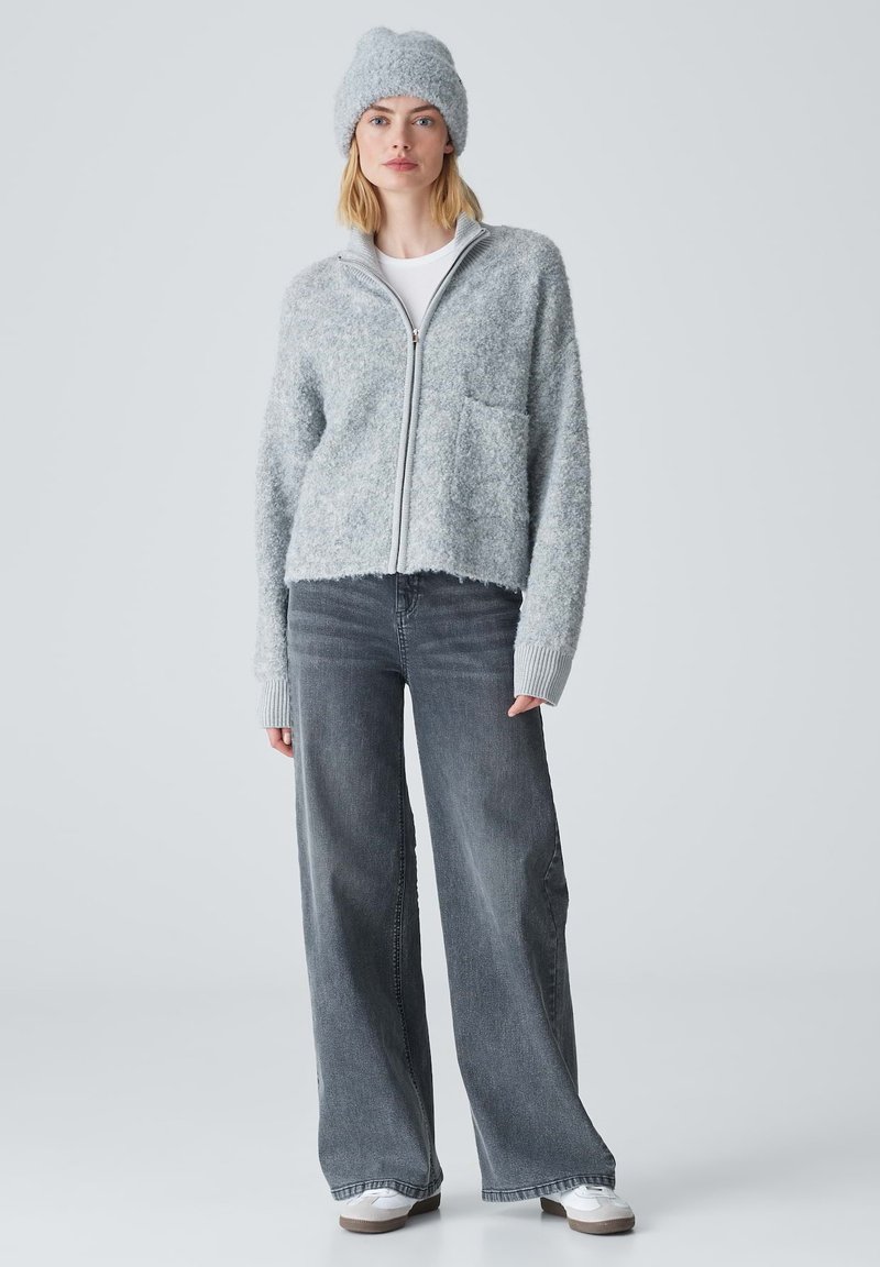 Light gray zip-up fuzzy cardigan with pocket, paired with high-waisted dark gray wide-leg jeans and a matching textured beanie.