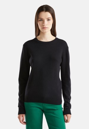 Maglione di lana nera con scollatura rotonda e maniche lunghe, caratterizzato da polsini e orlo a coste, abbinato a pantaloni verdi.