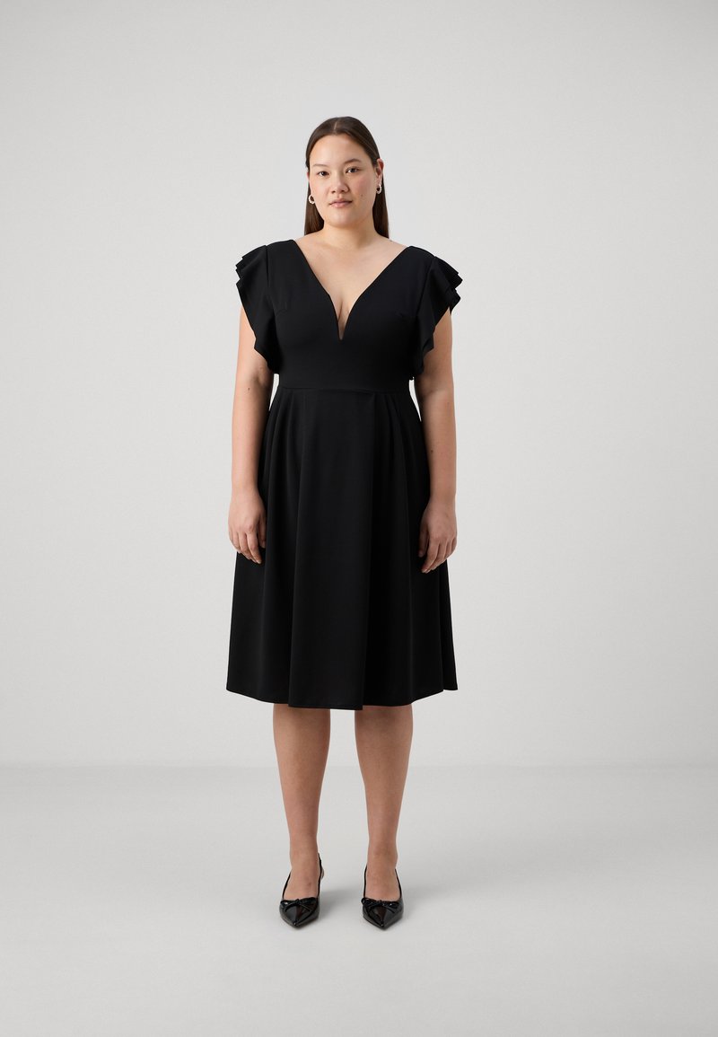 Vestido negro con escote en V profundo y mangas con volantes. Confeccionado en una tela suave, presenta un cuerpo ajustado y una falda acampanada. Combinado con tacones negros.