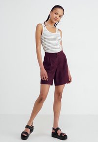 Hvit og marineblå stripete tank topp sammen med burgunder shorts. Modellen har på seg svarte platåsandaler. Glatt stoff og skreddersydd design.