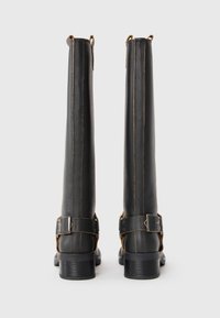 Botas de cuero negro hasta la rodilla con costuras marrones, hebillas laterales ajustables y un tacón sólido. Textura suave y diseño duradero.