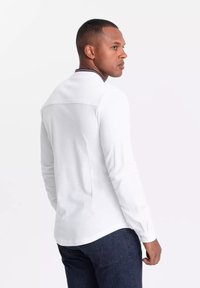 Camisa blanca de manga larga con cuello, con un acento de rayas rojas y marino; tela suave; diseño ajustado con un detalle de costura en la parte posterior.