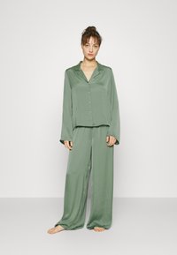 Grön satinpyjamas som består av en långärmad skjorta med knappar och löst sittande byxor med en slät textur och avslappnad silhuett.