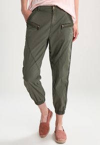 Olivgröna cargo-byxor med avsmalnande fållar, med två framfickor med dragkedja och diagonala sömsdekor. Tillverkade av lättviktig tyg.