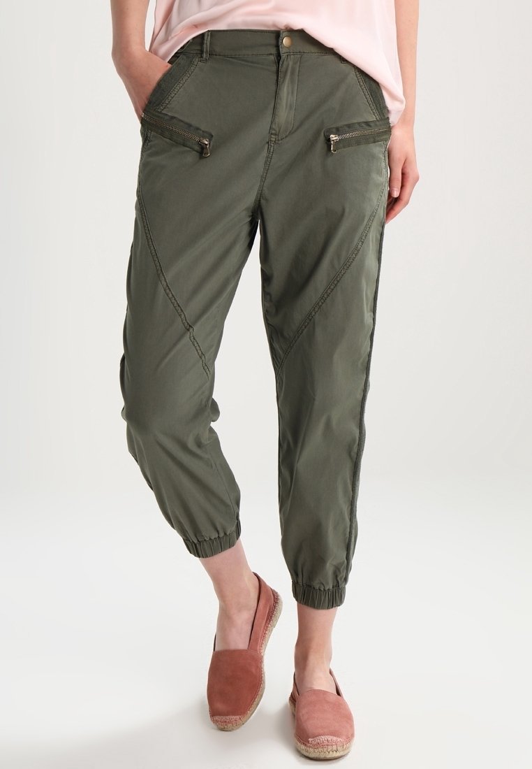 Olivgröna cargo-byxor med avsmalnande fållar, med två framfickor med dragkedja och diagonala sömsdekor. Tillverkade av lättviktig tyg.