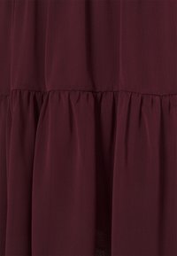 Dunkelburgunderfarbener Stoff mit gerafftem Volantdetail, das sanfte vertikale Falten und Textur erzeugt.