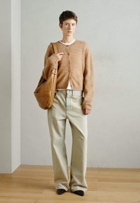 Μπεζ πλεκτό καρδιναλόν με στρογγυλά κουμπιά, λευκό μπλουζάκι, ανοιχτό τζιν παντελόνι σε άνοιγμα, και καφέ δερμάτινη τσάντα tote. Μαύρα μυτερά παπούτσια.