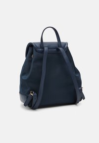 Granatowy plecak z gładkiego materiału o zaokrąglonym kształcie, z klapą na zamknięciu, dwoma ramiączkami i złotymi akcentami wykończenia.