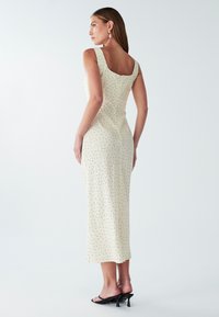 Kremasta midi haljina s crnim točkicama, kvadratnim izrezom, širokim naramenicama i prilagođenim siluetom. Glatka tkanina i suptilan sjaj.