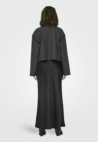 Abito lungo nero con silhouette aderente, abbinato a un giubbotto di lana grigio scuro corto, caratterizzato da un bordo testurizzato e maniche larghe.