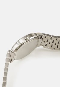Montre en métal avec un boîtier et un bracelet en acier inoxydable. Présente un cadran rond, une couronne texturée et une finition polie.