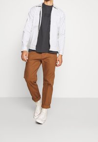 Paski biała kurtka na suwak na szarym t-shircie, zestawiona z brązowymi spodniami i białymi trampkami. Charakteryzuje się casualowym, luźnym krojem.