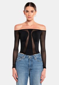 Schwarzer Off-Shoulder-Bodysuit mit transparenten langen Ärmeln, figurbetontem Schnitt und stilvollen transparenten Einsätzen, kombiniert mit hellblauen Jeans.