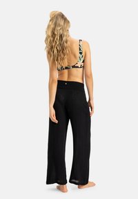 Bralette con stampa floreale e spalline spesse abbinato a pantaloni neri larghi e texturizzati con vita elasticizzata, visti da dietro.