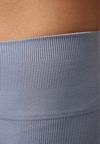 Tessuto a coste blu chiaro con un punto vita strutturato, vista ravvicinata che mette in evidenza la sua elasticità e i contorni sulla tonalità della pelle.