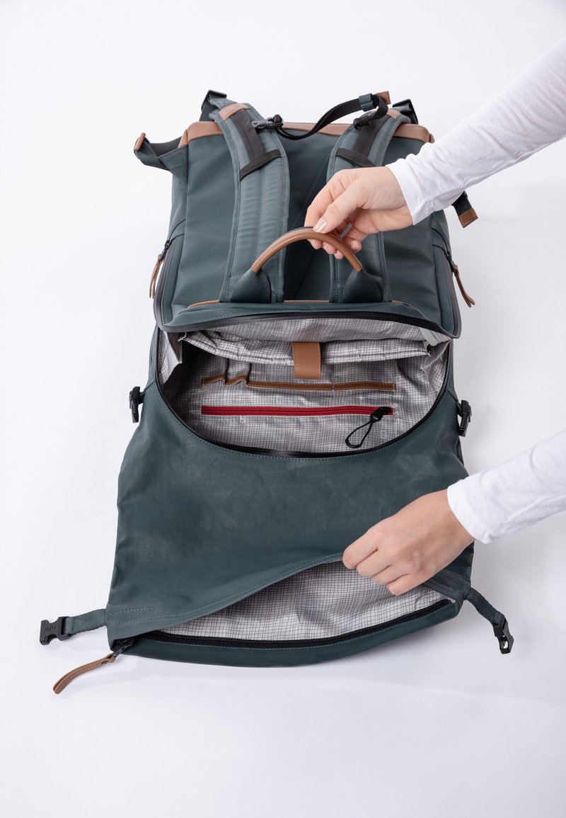 Rucksack mit grünem Äußeren, beigen Akzenten und einem Reißverschlussfach. Das Innere verfügt über grauen karierter Stoff und Organisationsfächer.
