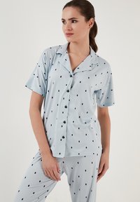 Světle modrý pyžamový set se sepraným vrškem na knoflíky s krátkým rukávem a námořnickými puntíky, doplněný o odpovídající kalhoty. Měkká, hladká tkanina s volným střihem.