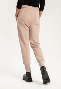 Beiga joggerbyxor gjorda av mjukt tyg, med ribbad midja, sidofickor och manschettavslut. Bärs med svarta ankelboots.