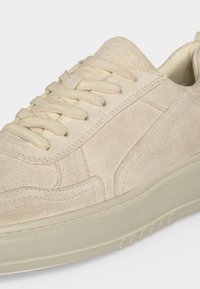 Μπεζ σουέντ αθλητικό παπούτσι με παχιά λαστιχένια σόλα, ραμμένες λεπτομέρειες και μπεζ κορδόνια σε λευκό φόντο.