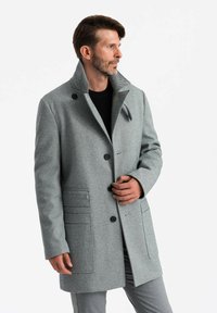 Abrigo de mezcla de lana gris con un cuello alto, cierre de botones y dos bolsillos frontales que presentan un sutil patrón de espiga.