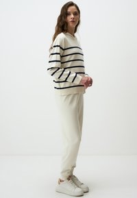 Cream-colored, striped sweater with navy lines; paired with matching cream joggers and white sneakers with tan accents. Simple, casual design.