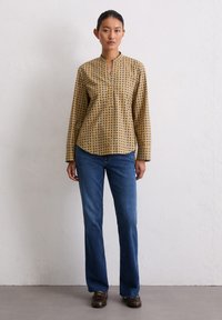 Langsleeve, mosterdgele blouse met een blauw geometrisch patroon, voorzien van een v-hals en een relaxte pasvorm, gecombineerd met rechte blauwe jeans.