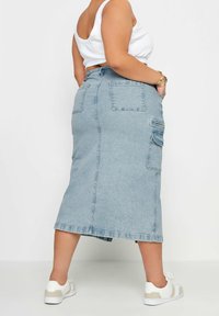 Ljusblå denim midi kjol med två bakfickor och sidokargo fickor, avslutad med rå nederkant. Bärs med ett vitt linne och sneakers.