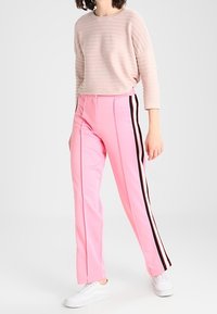 Rosa Hosen mit seitlichen schwarzen Streifen, gerader Schnitt und glatter Textur, kombiniert mit einem hellrosa gerippten Oberteil. Weiße Sneakers dazu getragen.