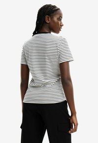Camiseta de manga corta a rayas en algodón negro y blanco con cuello redondo y corte relajado, combinada con pantalones negros.