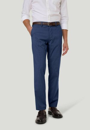 Blaue gemusterte Hose aus Stoff mit strukturiertem Finish, getragen mit einem weißen Hemd mit Knöpfen und einem braunen Ledergürtel. Braune Schuhe runden den Look ab.