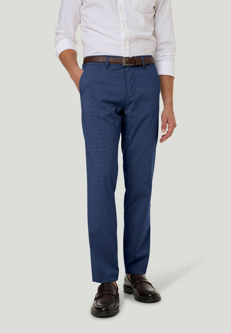 Blaue gemusterte Hose aus Stoff mit strukturiertem Finish, getragen mit einem weißen Hemd mit Knöpfen und einem braunen Ledergürtel. Braune Schuhe runden den Look ab.