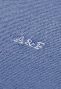 Tissu en coton bleu clair à texture lisse, orné de lettres blanches brodées "A&F" dans une police détendue et décontractée.