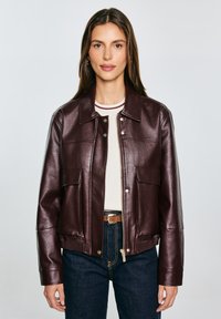 Burgunderfarbene Lederjacke mit kragenförmigem Ausschnitt, Frontdruckknopf- und Reißverschluss, zwei Taschen und geripptem Saum; kombiniert mit einem gestreiften Oberteil und Jeans.