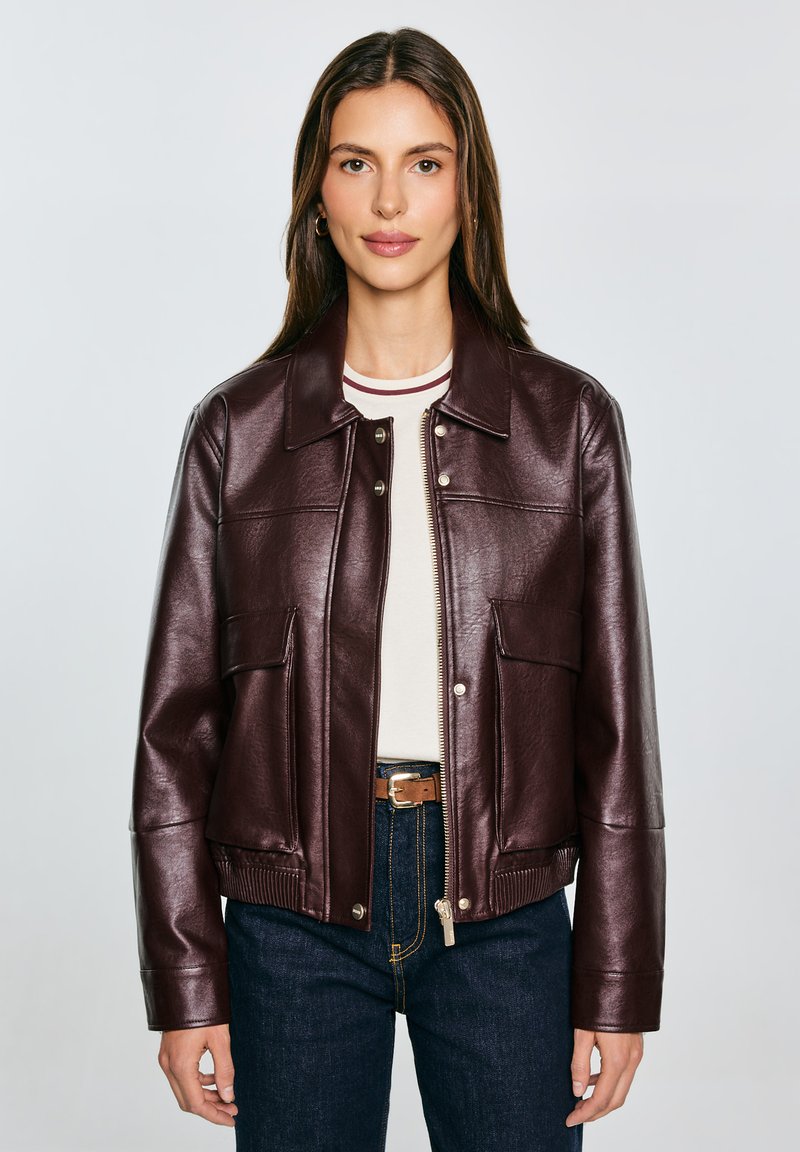 Burgunderfarbene Lederjacke mit kragenförmigem Ausschnitt, Frontdruckknopf- und Reißverschluss, zwei Taschen und geripptem Saum; kombiniert mit einem gestreiften Oberteil und Jeans.