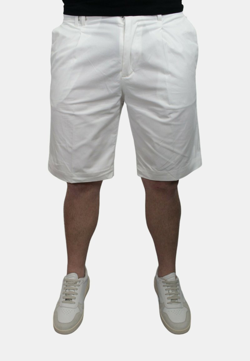 Pantaloni corti bianchi realizzati in tessuto leggero, caratterizzati da una parte anteriore piatta, tasche laterali e un taglio pulito. Abbinati a sneaker di colore chiaro.